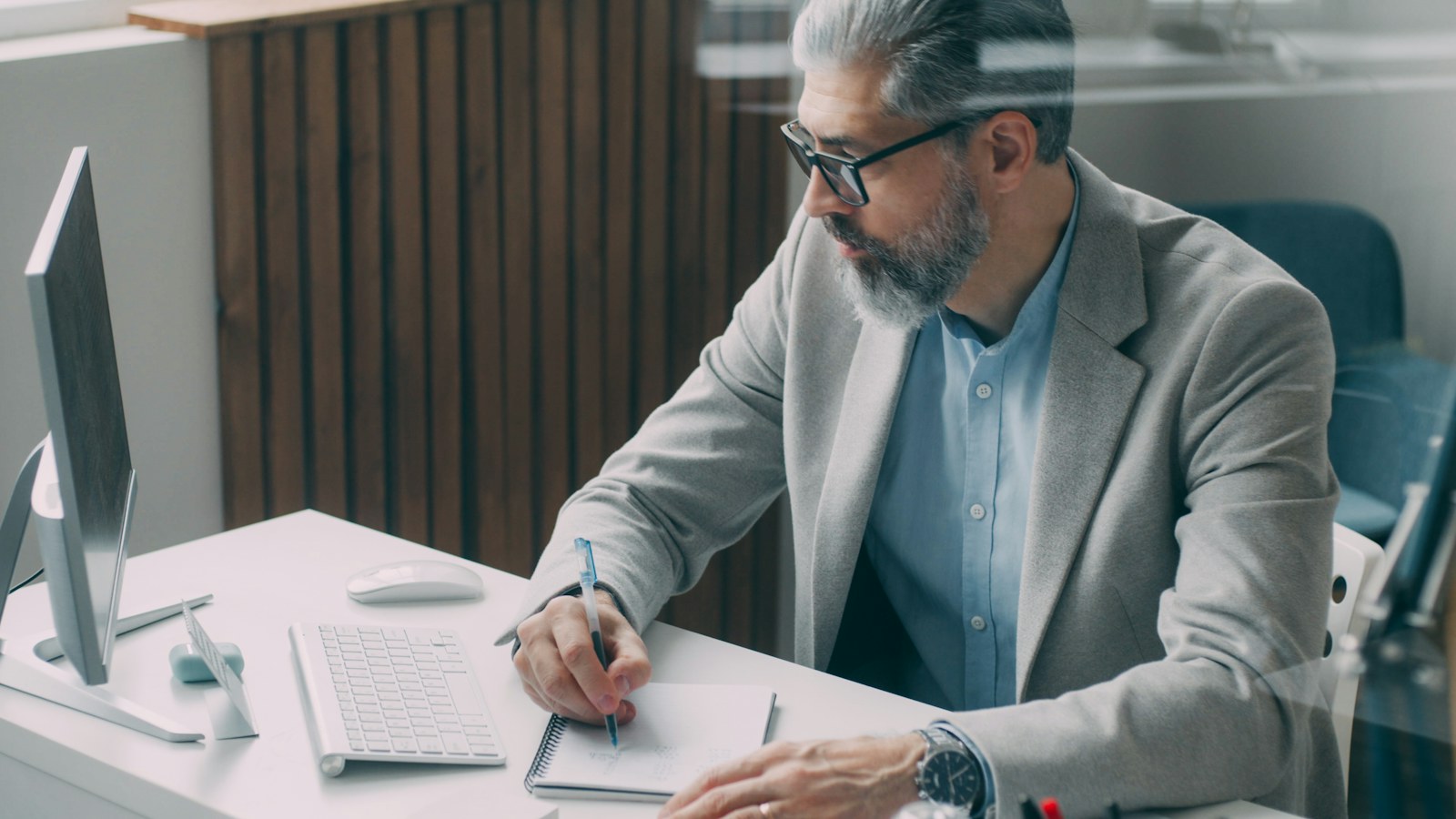 An experienced credit manager in glasses writing a note on a customer file beside his monitor, the point at which a past due account is put on credit hold
