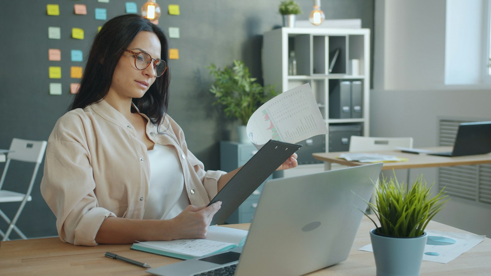 A credit manager at an office desk reviewing a printed accounts receivable performance report beside a laptop